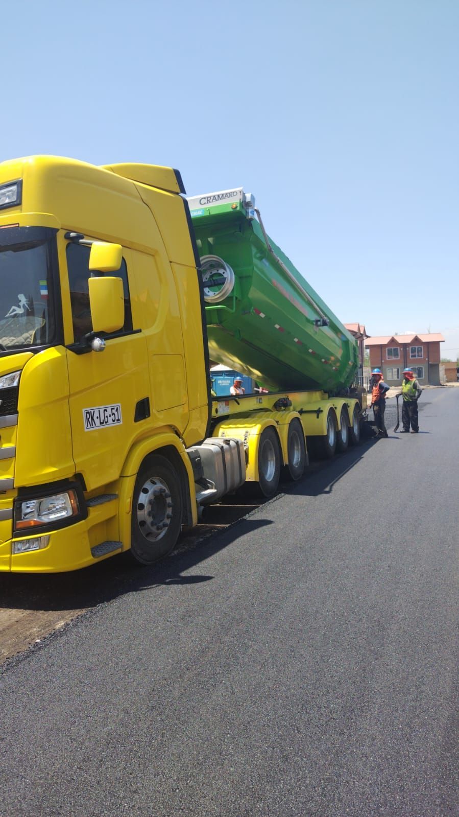 Asfaltos Patricio Contreras - Un camión amarillo con un remolque verde está estacionado depositando el concreto en el piso.