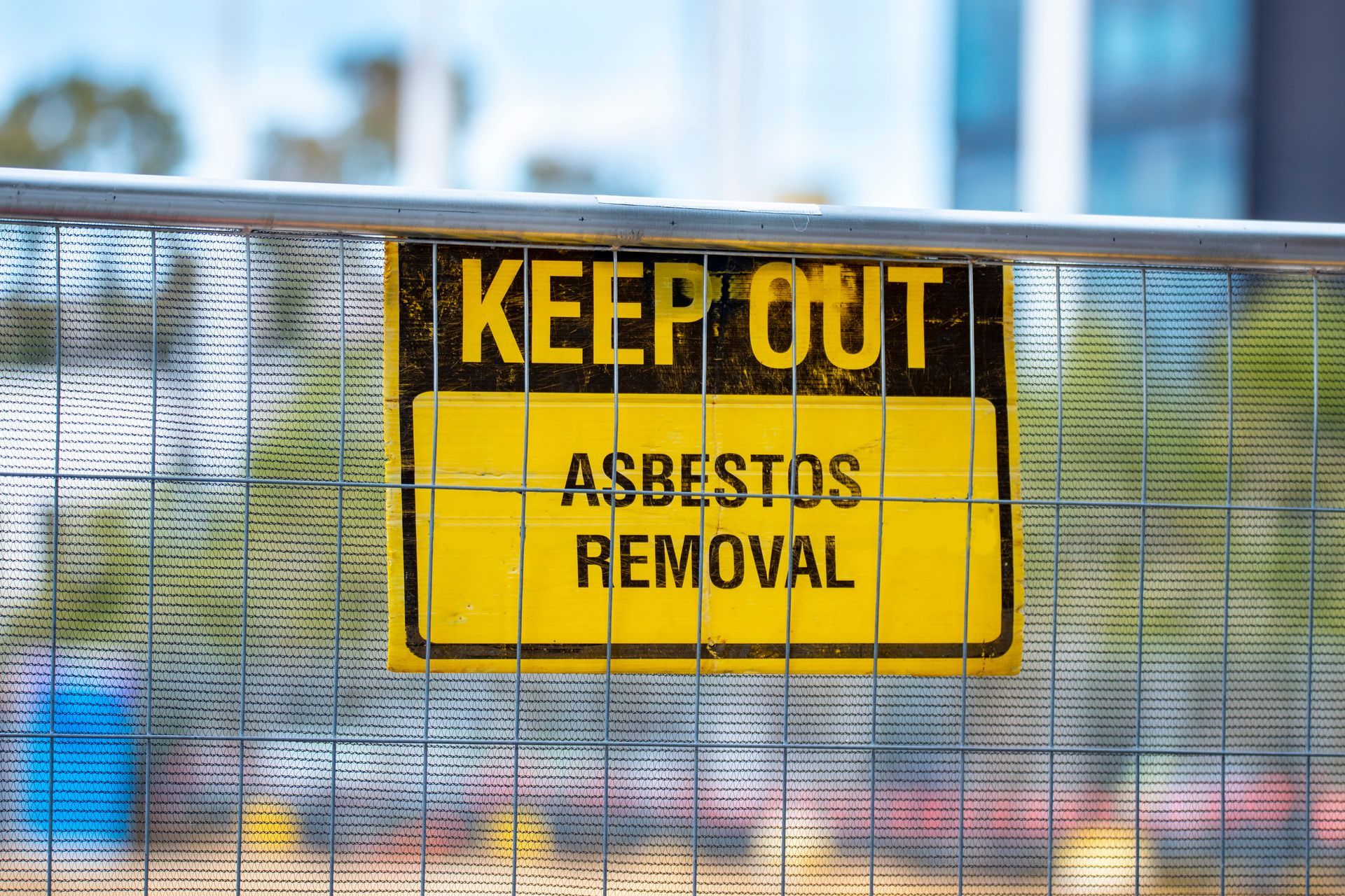 Yellow “Keep Out – Asbestos Removal” sign attached to a metal fence at a work site. Yellow “Keep Out – Asbestos Removal” sign attached to a metal fence at a work site.