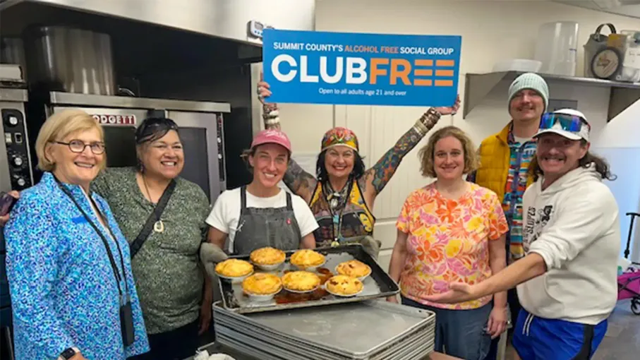 A group of people are standing in a kitchen holding a club free sign.