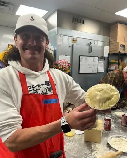 A man in an apron is holding a pie in his hands.