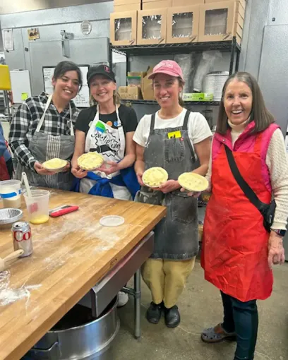 A group of women are standing in a kitchen holding pies.