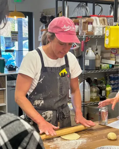 A woman wearing a pink hat is rolling dough on a table.