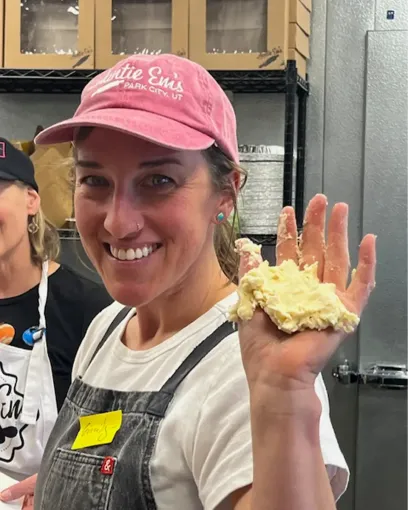 A woman wearing a pink hat holds a piece of dough in her hand