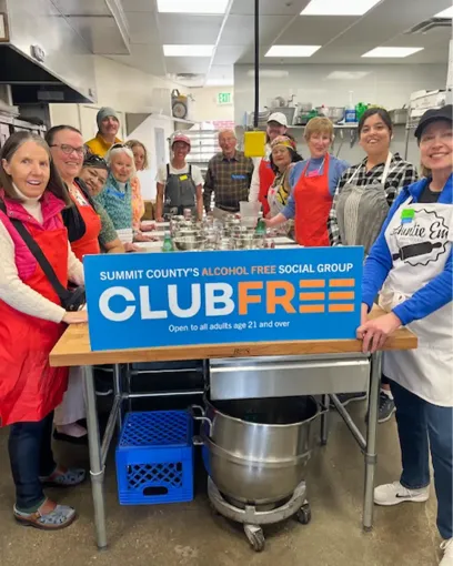 A group of people are standing in a kitchen holding a club free sign.