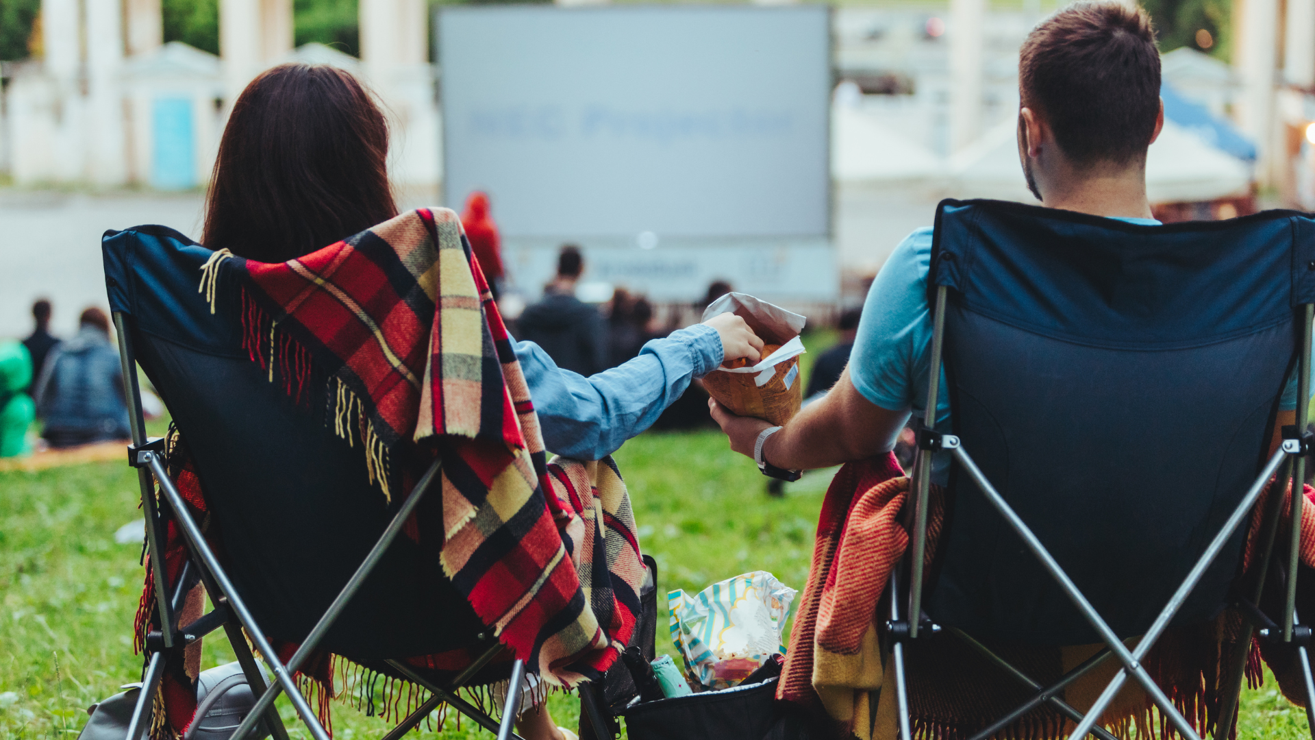 Image of two individuals sitting on camp chairs in a field of grass.