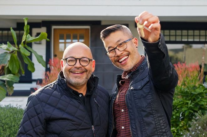 Two men smiling in front of a house; one holds up a key.