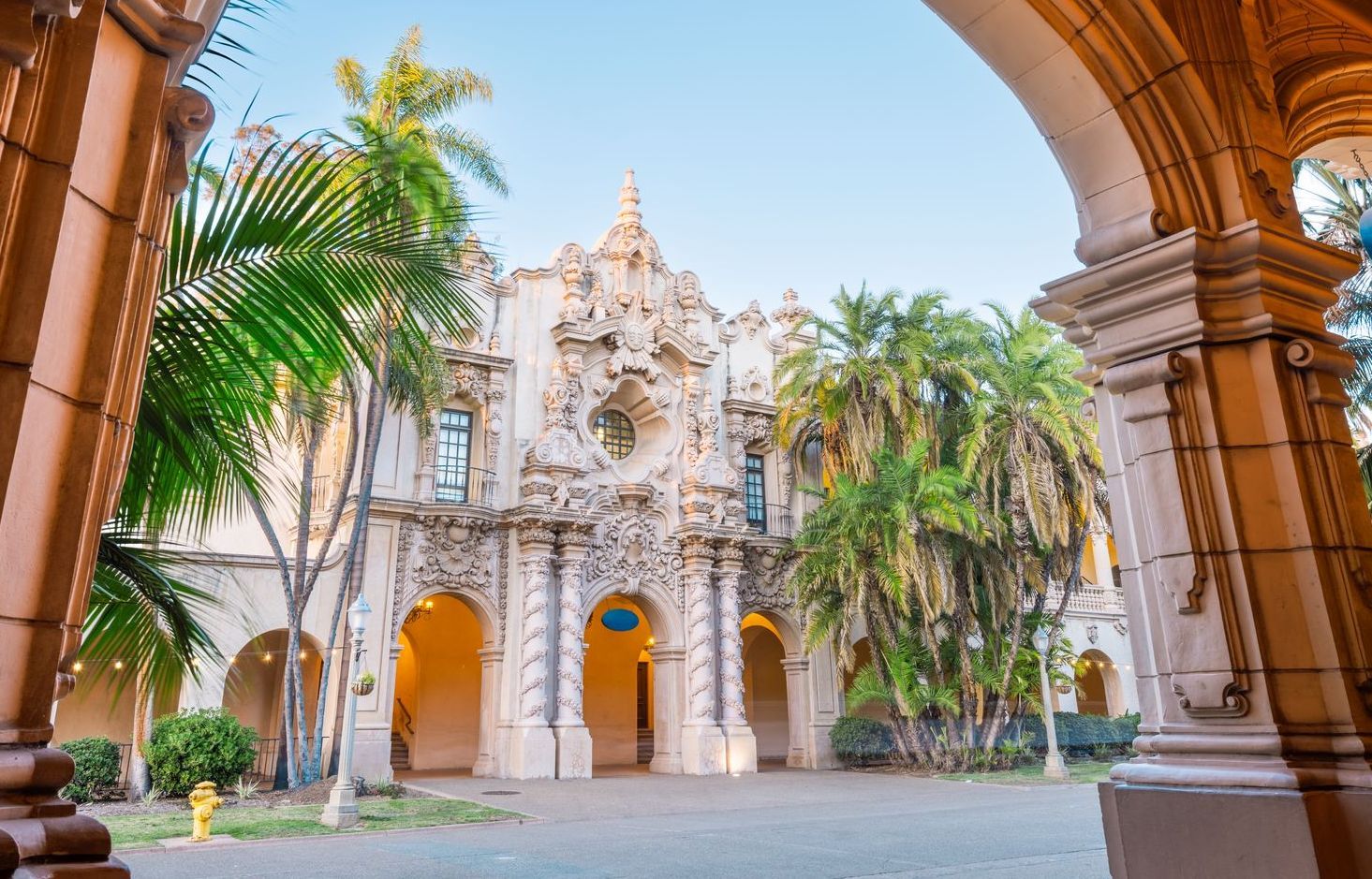 Ornate Spanish-style building with arched doorways and detailed facade, palm trees, and a clear sky.