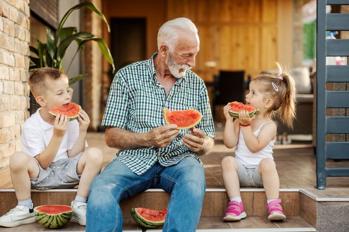 Grandfather and two grandchildren eating watermelon on porch steps.