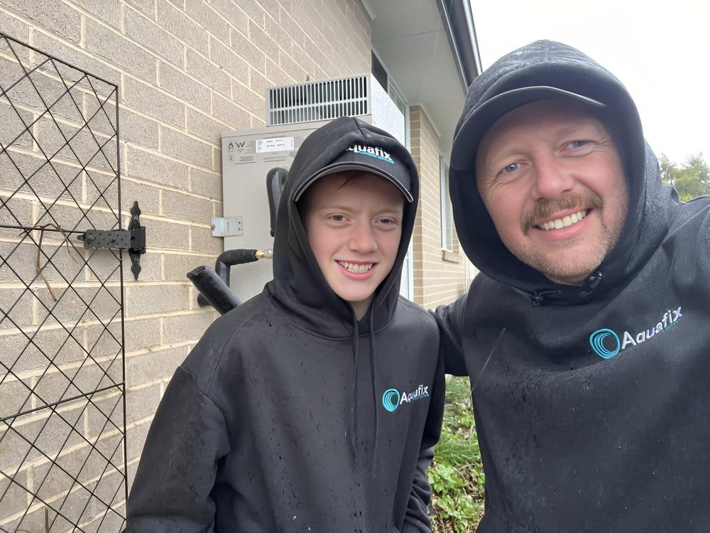 A Man And A Boy Are Posing For A Picture In Front Of A Brick Wall — Aquafix Plumbing Services in Bowral, NSW