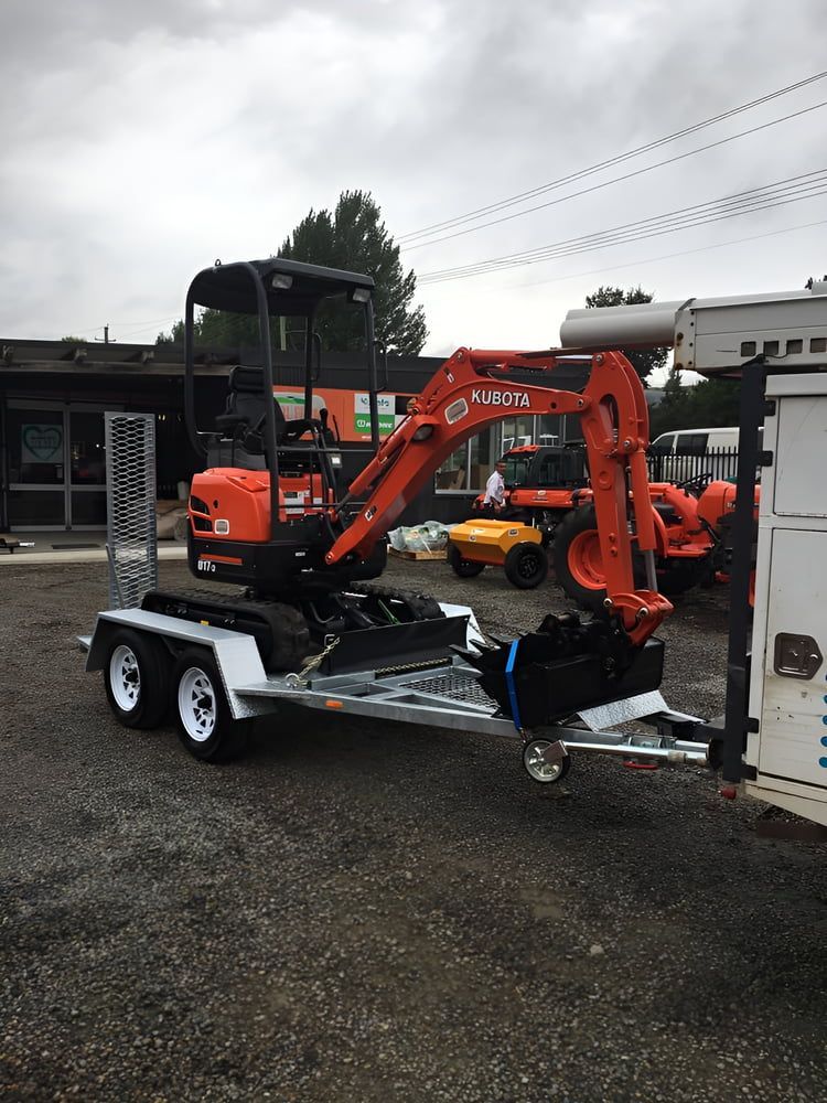 A Small Excavator Is On A Trailer In A Parking Lot — Aquafix Plumbing Services in Bowral, NSW