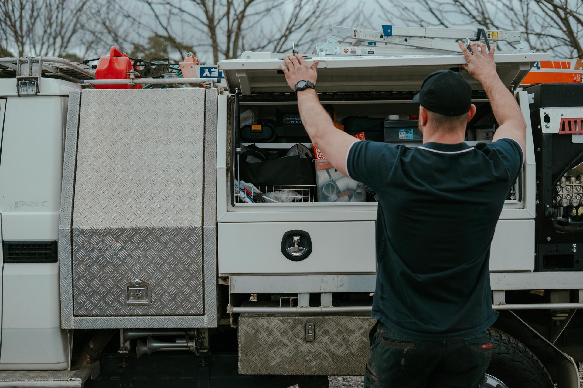 Worker opening a utility truck compartment with tools and equipment visible inside — Aquafix Plumbing Services in Bowral, NSW
