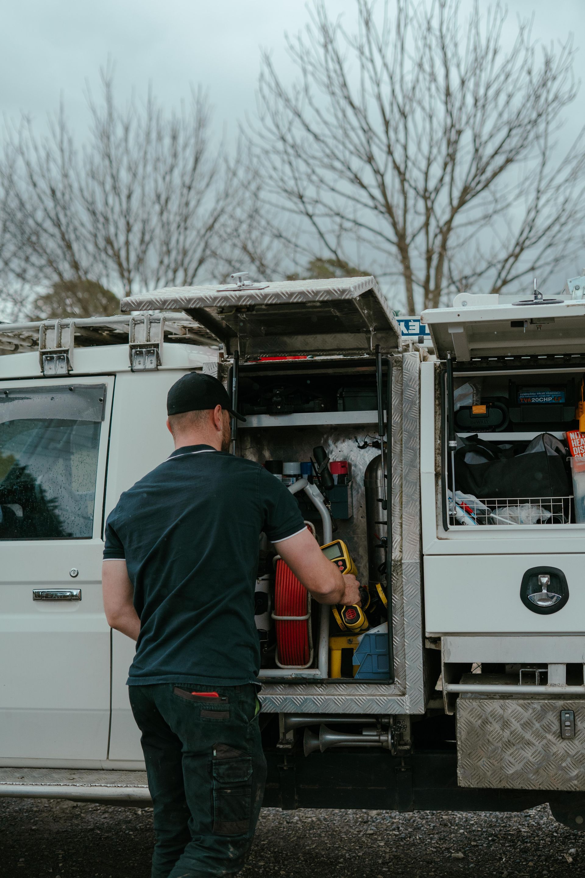 Man loading equipment into an open white utility van in a snowy outdoor lot — Aquafix Plumbing Services in Bowral, NSW