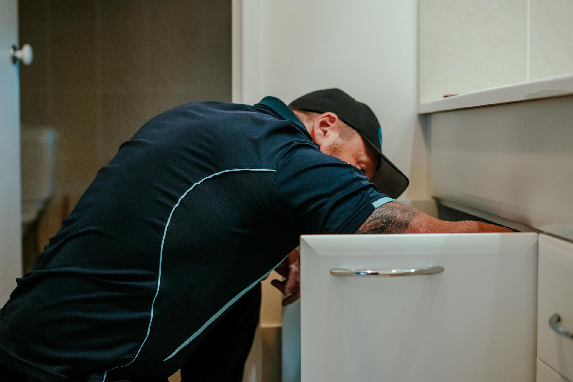 Technician in dark uniform leaning into a cabinet, working on something inside a room. — Aquafix Plumbing Services in Bowral, NSW