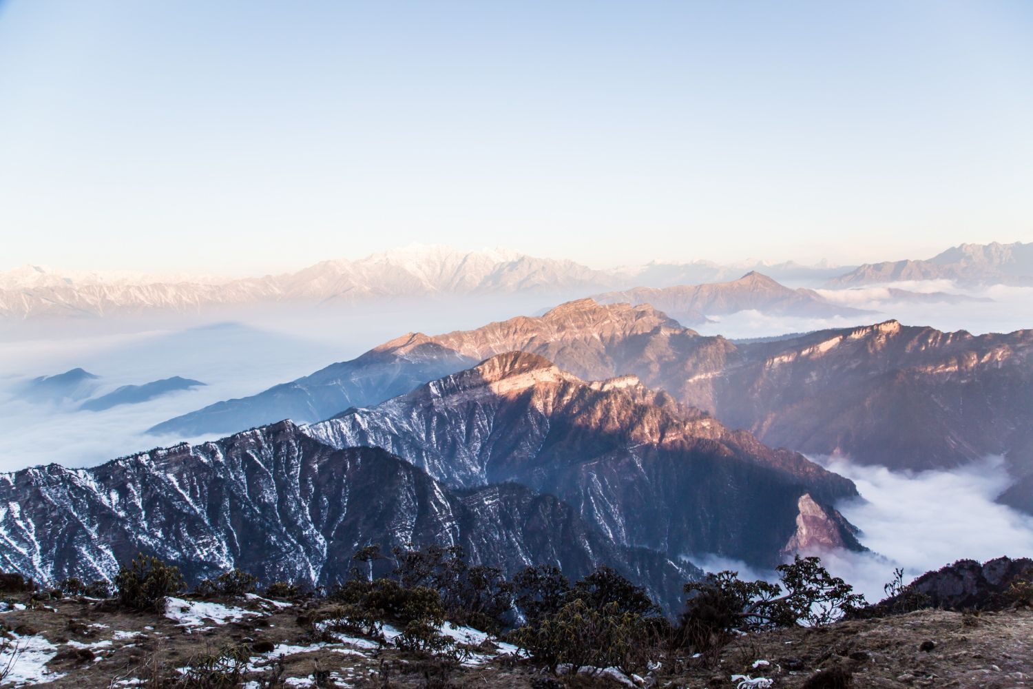 Mountains with snow-covered peaks, illuminated by golden sunlight; a sea of clouds fills the valleys below.