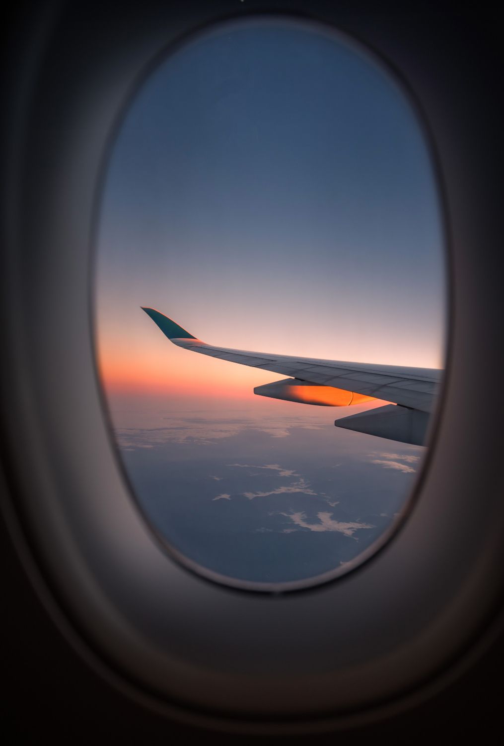 Airplane wing silhouetted against a colorful sunset visible through a plane window.