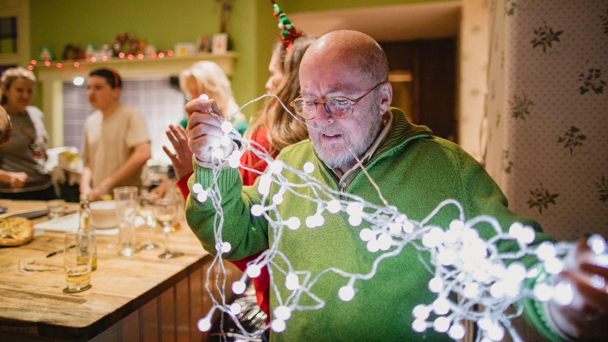 A man in a green sweater is holding a string of christmas lights.