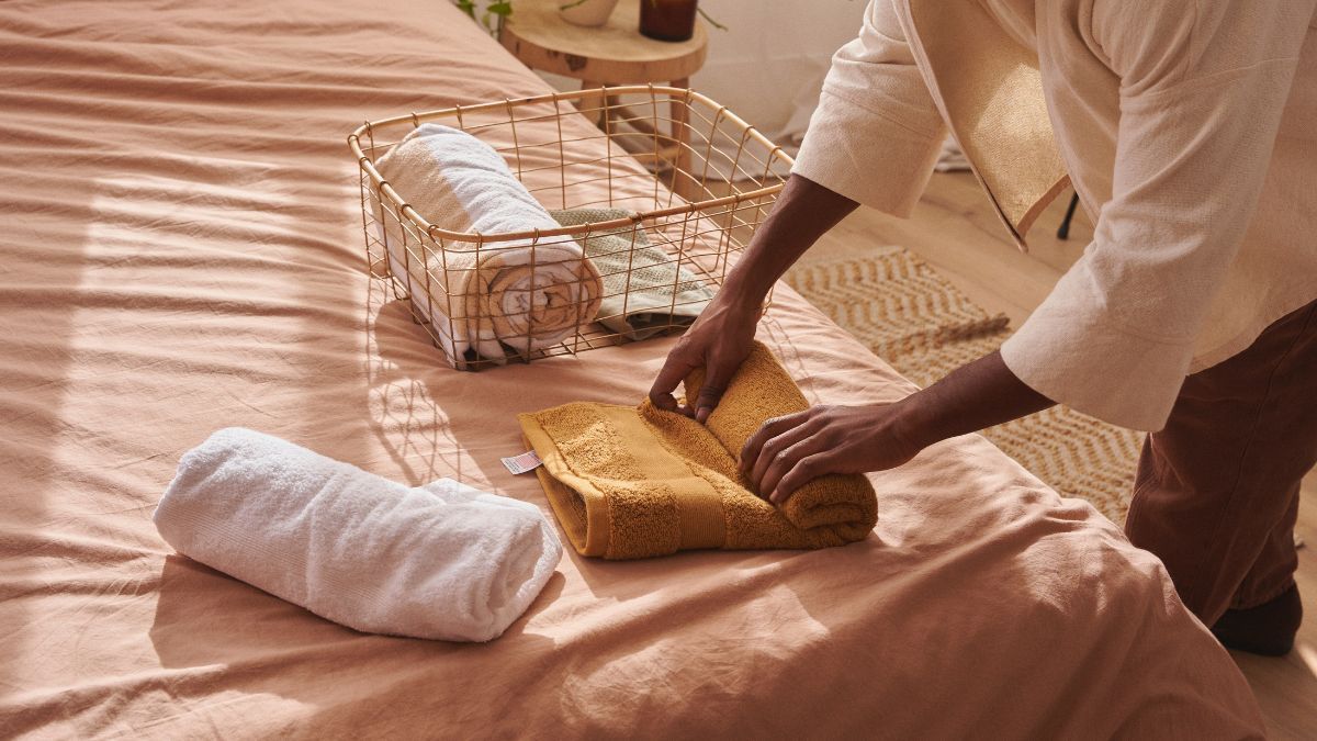 Woman is folding towels on a bed.