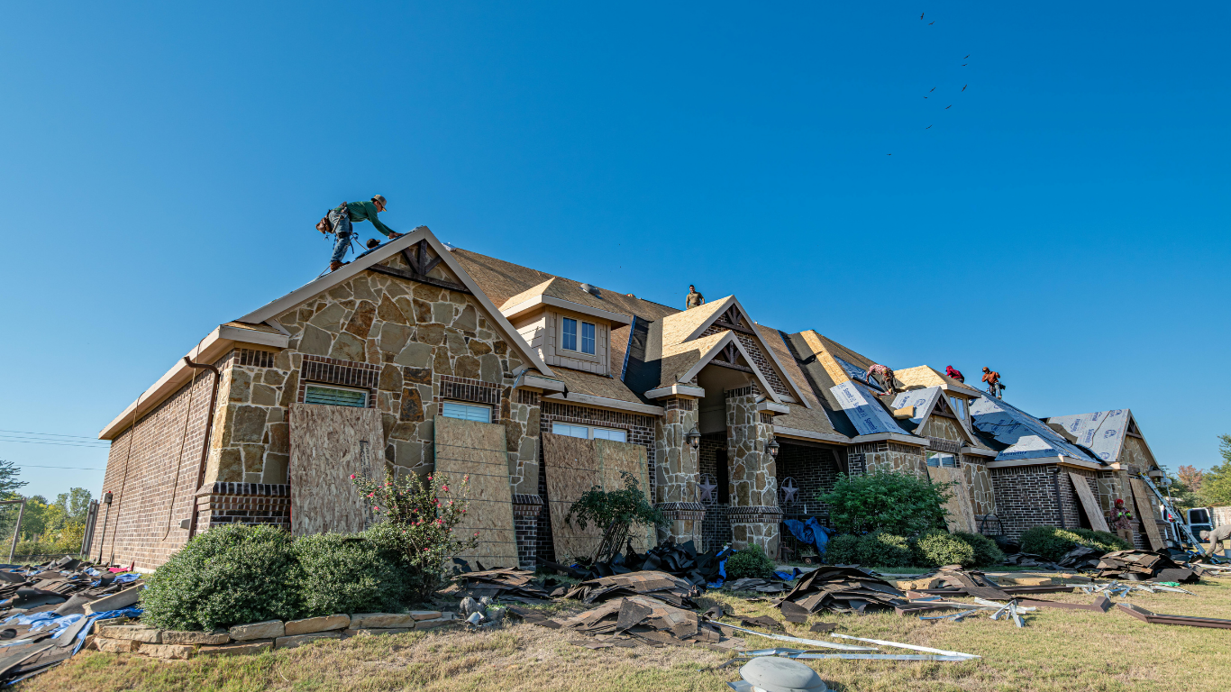 Construction workers on a house with exposed siding and roofing. Bright blue sky overhead.