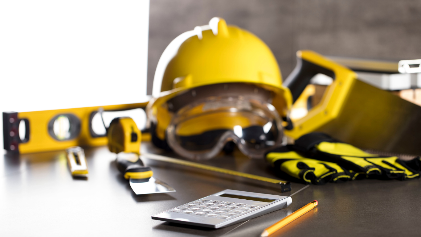 Yellow hard hat, safety glasses, tools, and calculator on a work surface.