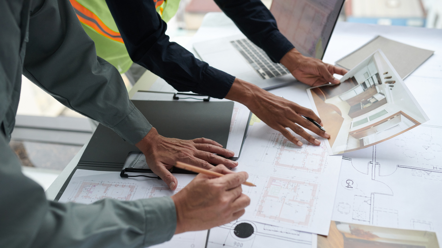 People reviewing architectural plans, using a laptop and a 3D rendering of a room.