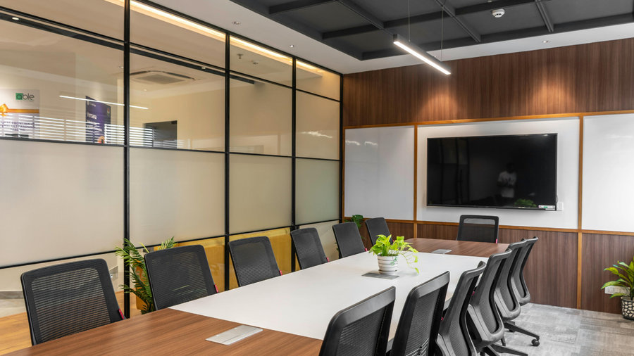 Conference room with long table, black chairs, glass wall, wood paneling, and a large TV.
