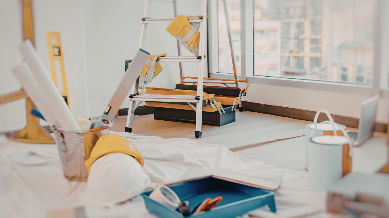Room under renovation with ladder, tools, paint supplies, and blueprints.