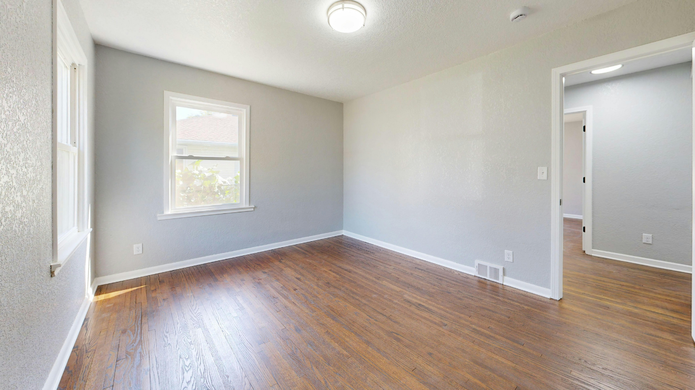 Empty room with hardwood floors, light gray walls, window, and doorway.