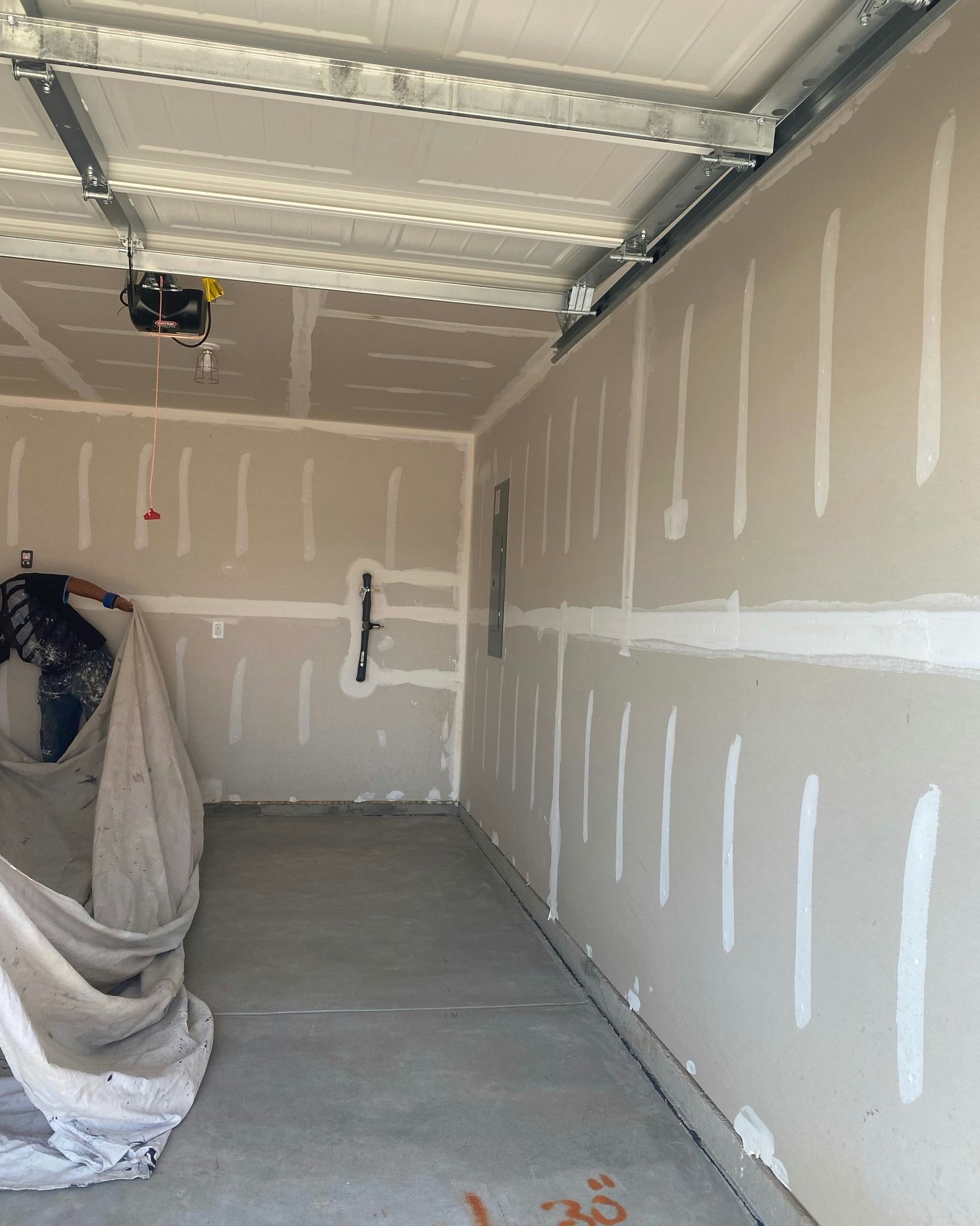 A garage interior under construction; drywall installed on walls; concrete floor.