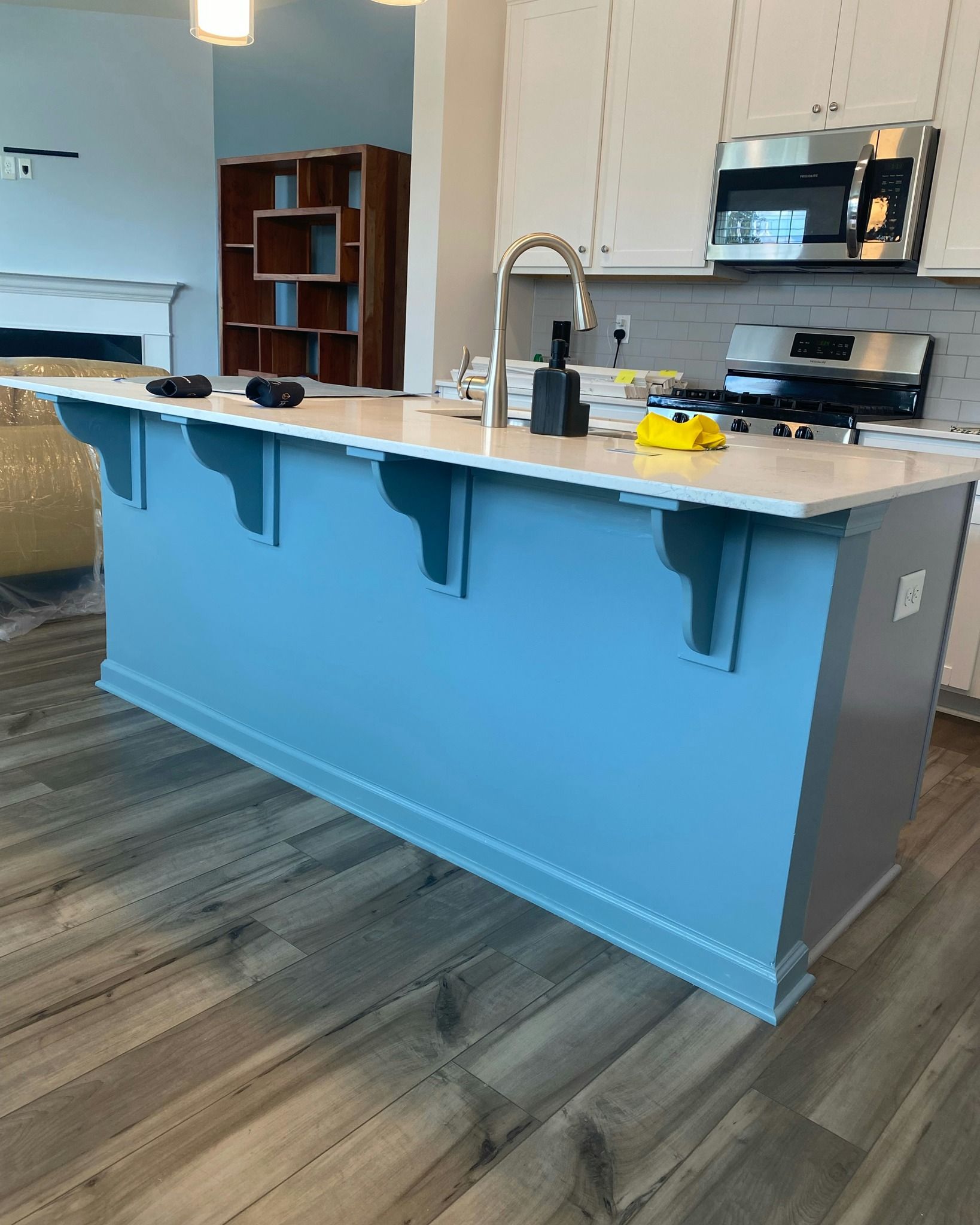 Blue kitchen island with light countertops and decorative supports, in front of wood flooring.