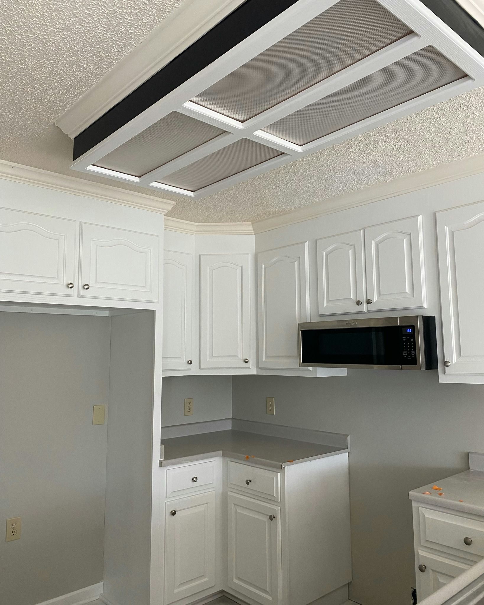 White kitchen with cabinets, microwave, and a ceiling light fixture.