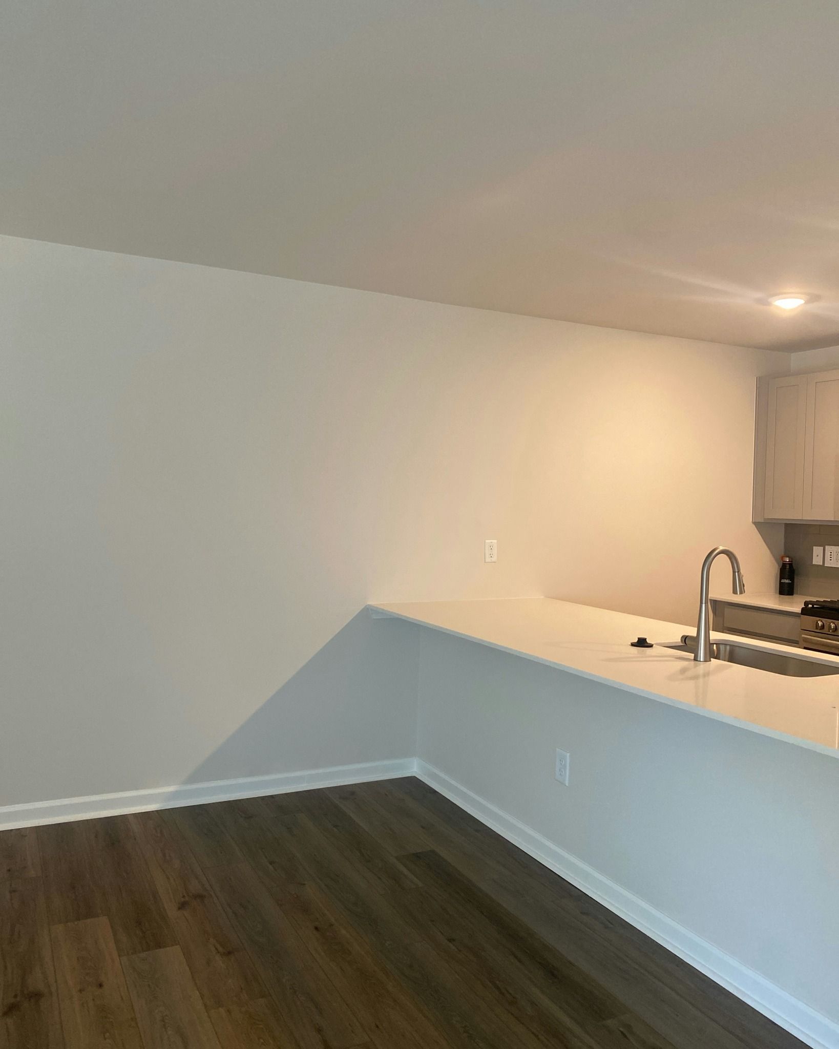 Kitchen with white countertop, cabinets, and wall. Dark wood floor.
