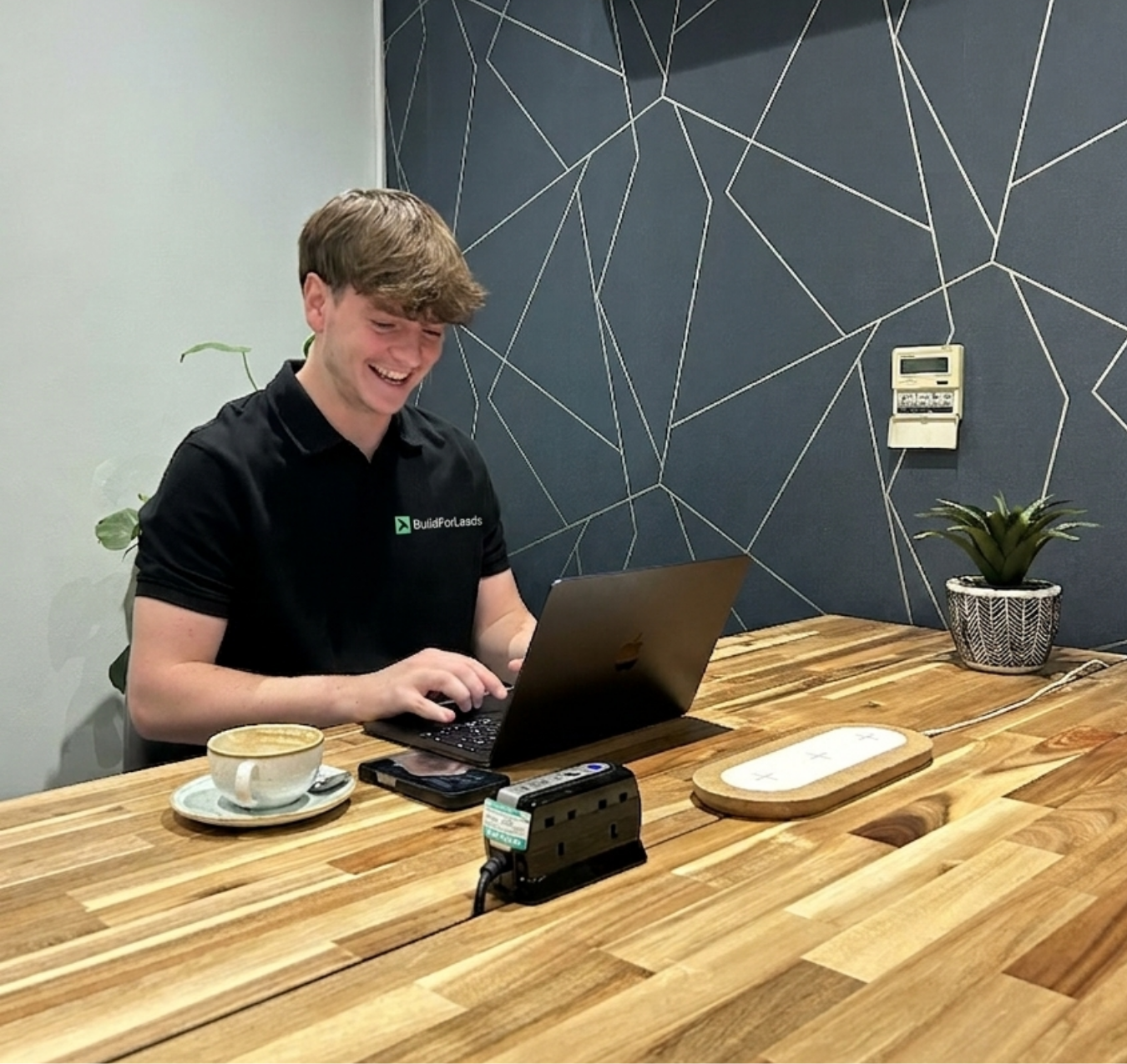 Two people talking at a table, one pointing at a laptop screen in a café setting.