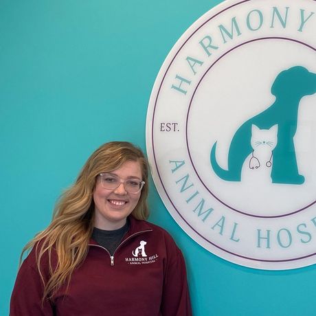 A woman is standing in front of a sign for harmony hill animal hospital