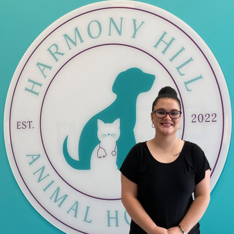 A woman is standing in front of a sign for harmony hill animal hospital