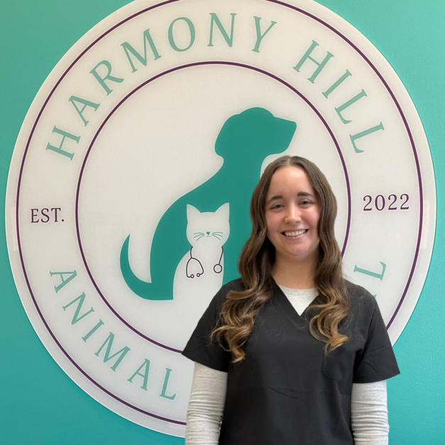 A woman is standing in front of a sign for harmony hill animal hospital