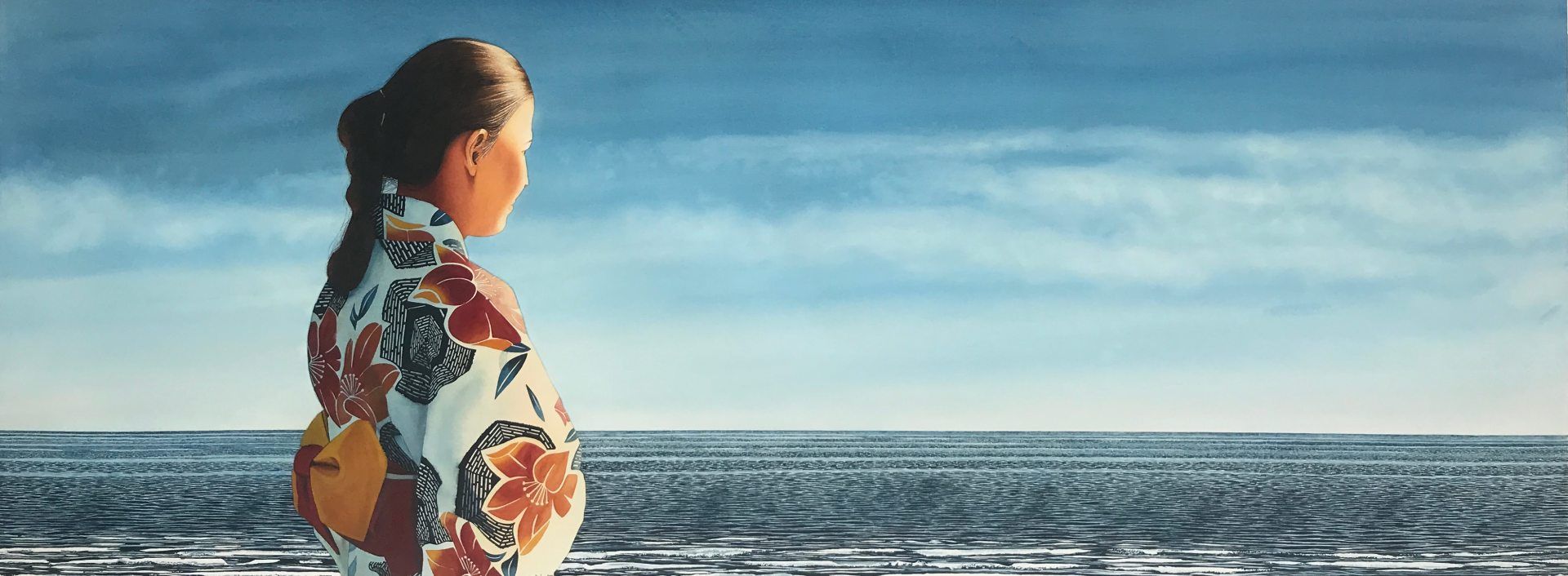 A woman in a kimono is standing on the beach looking at the ocean.