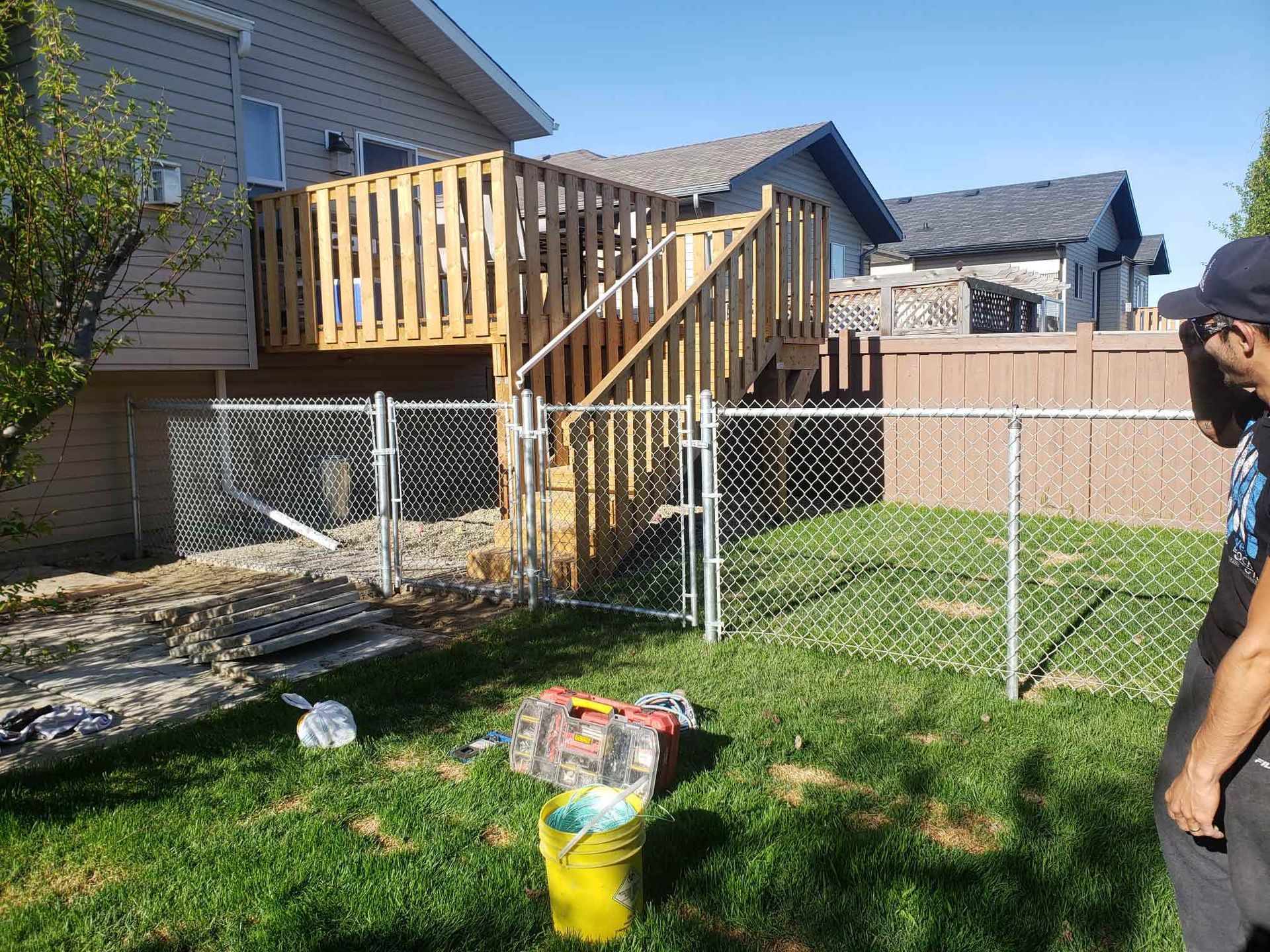 A man is standing in front of a chain link fence in a backyard.