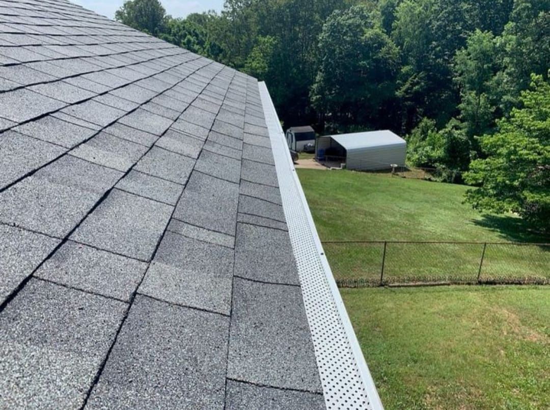 A roof with a gutter on it and a fence in the background.