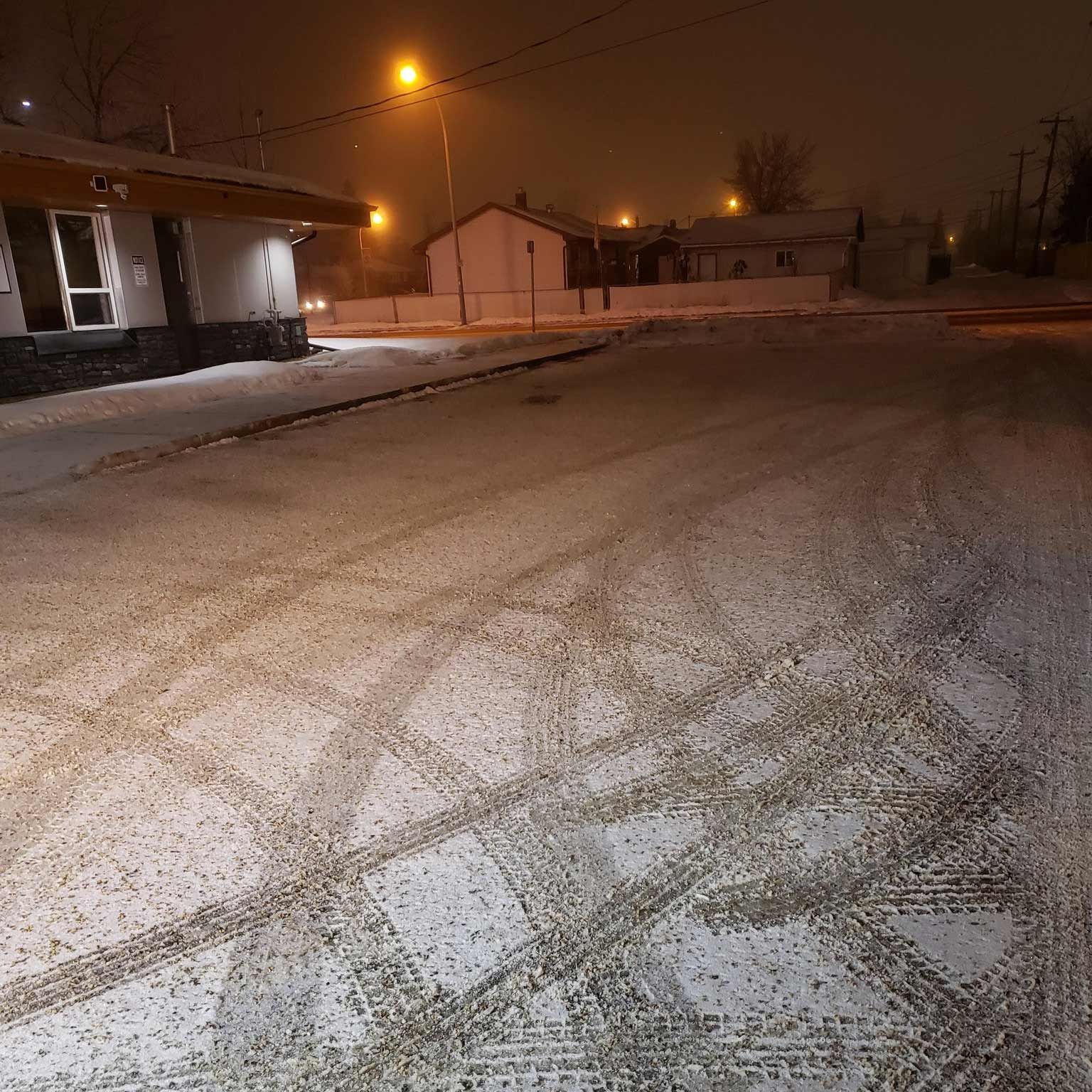 A snowy street with a building in the background at night