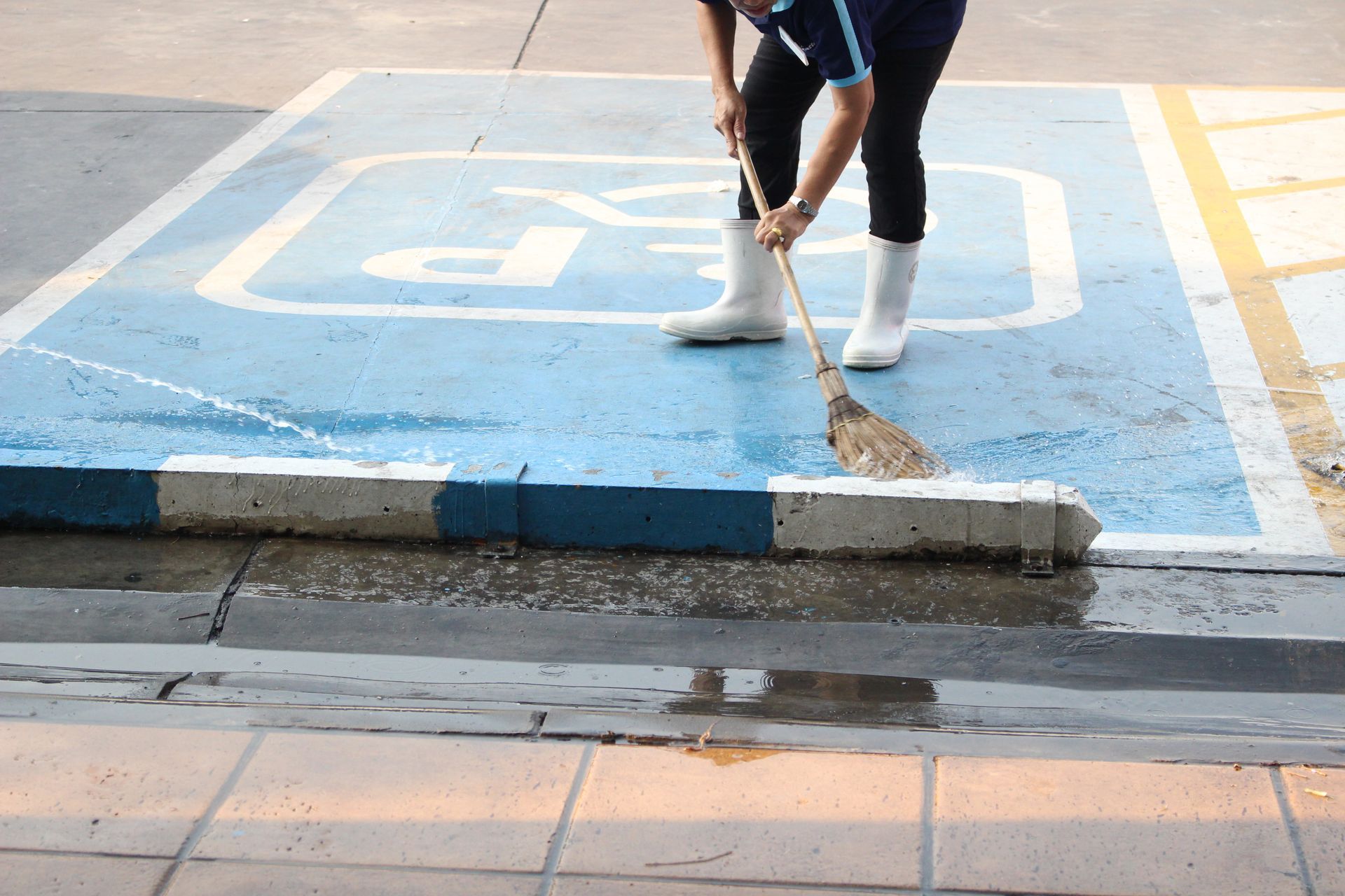 A person is sweeping a handicapped parking spot with a broom.