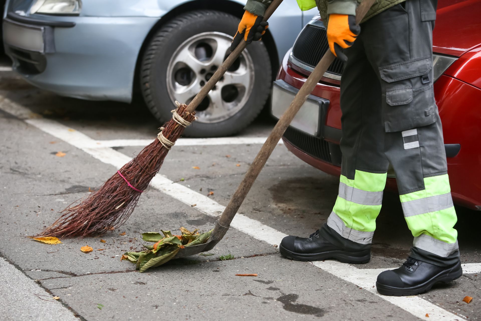 A man is sweeping the ground with a broom in a parking lot.