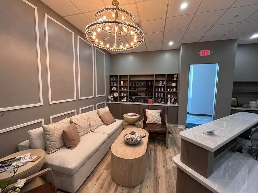 Salon waiting area with beige couch, wooden table, and decorative lighting.