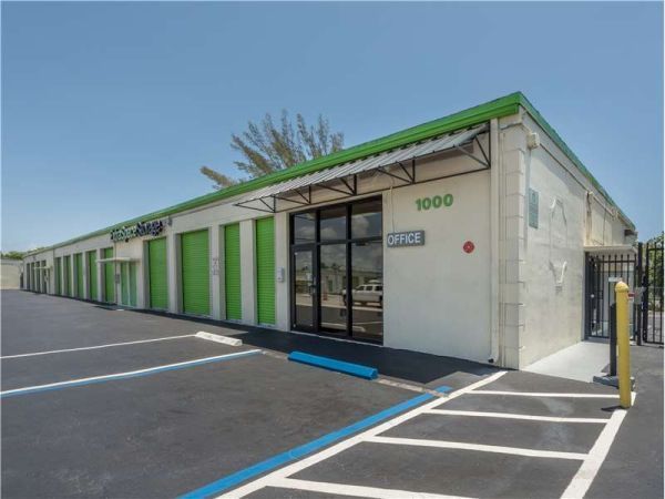 Exterior of a storage facility with green doors, office, and parking under a blue sky.