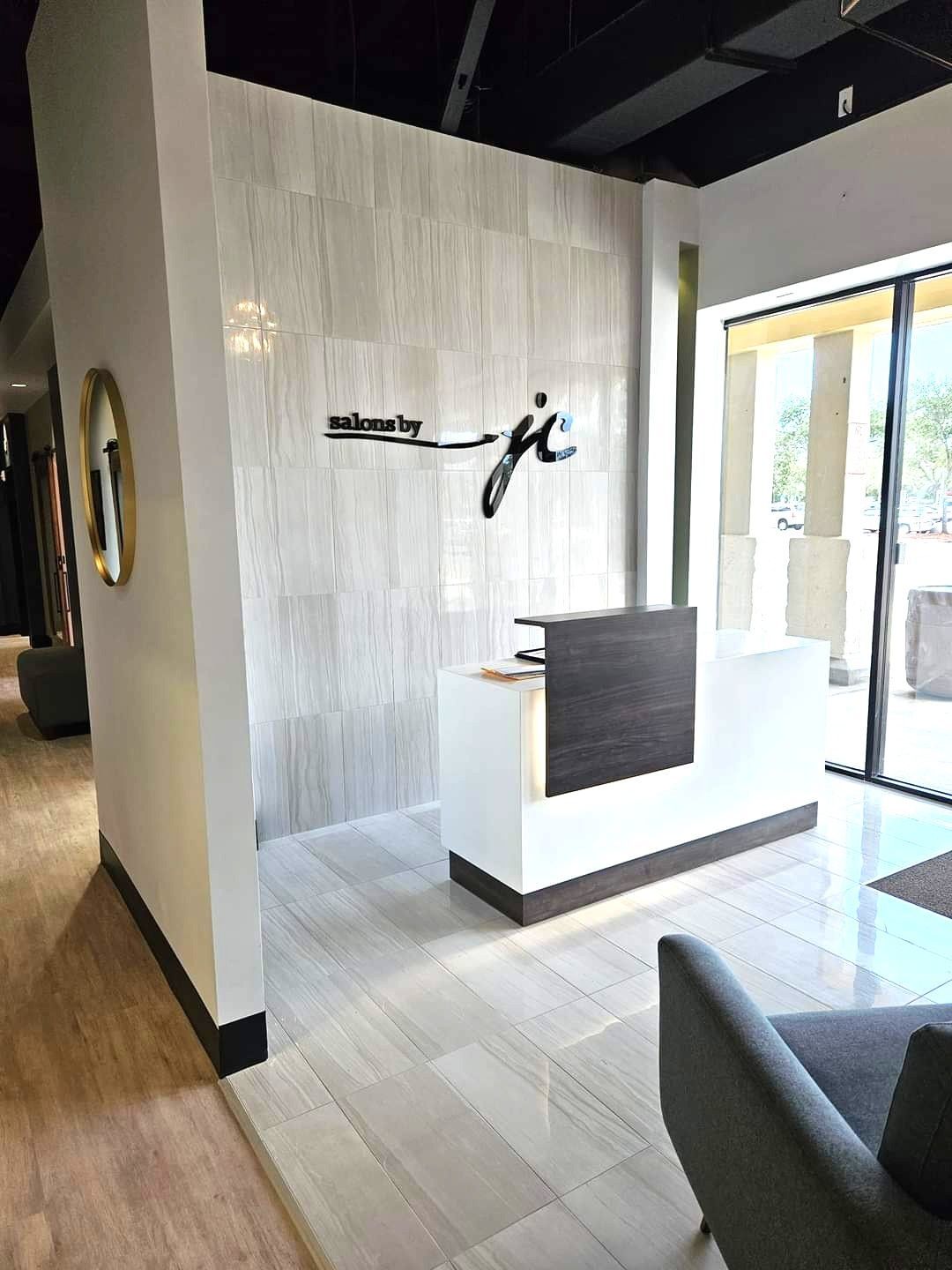 Modern office reception area with white and gray decor; a white desk with dark wood accent and a logo on the wall.