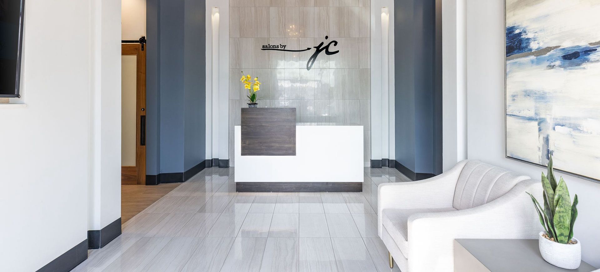 Modern office lobby with reception desk, white walls, and a waiting area with a sofa.