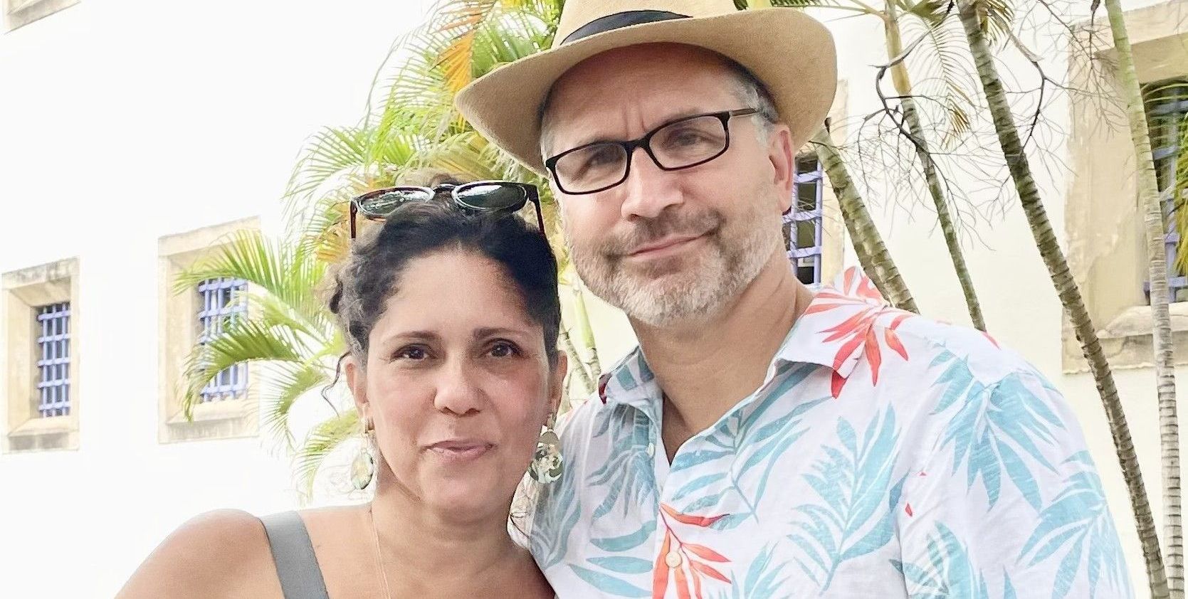 A man and a woman are posing for a picture together . the man is wearing a hat and glasses.