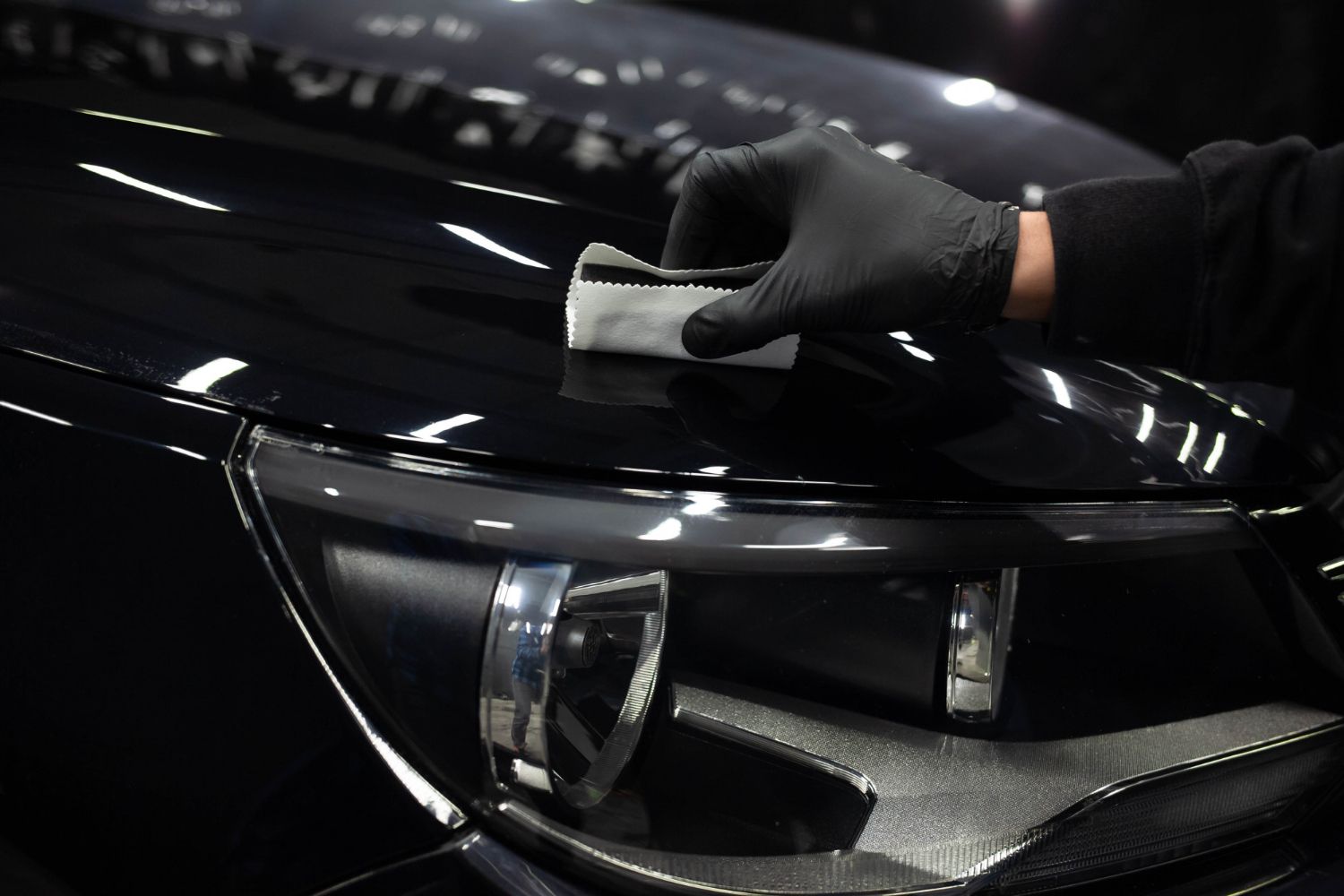 A person is cleaning the hood of a car with a towel.