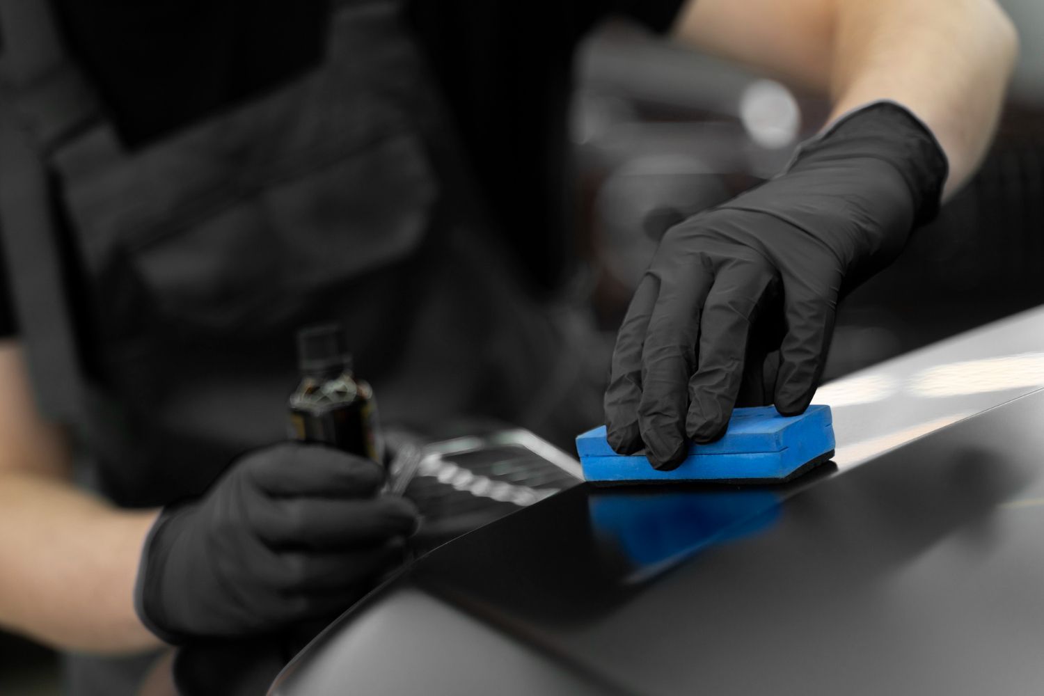 A man is cleaning the hood of a black car with a cloth.