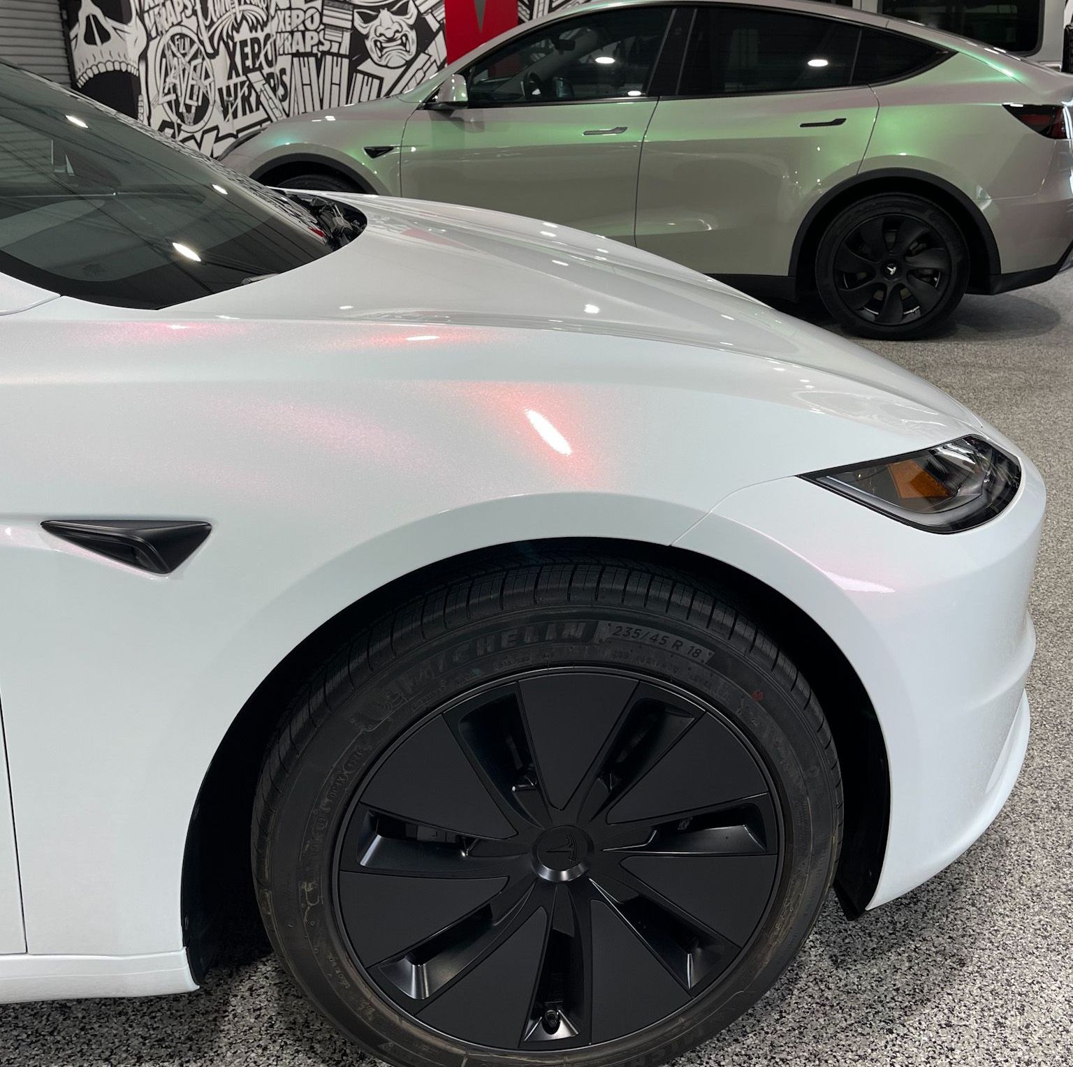 A white car with black wheels is parked next to a green car.