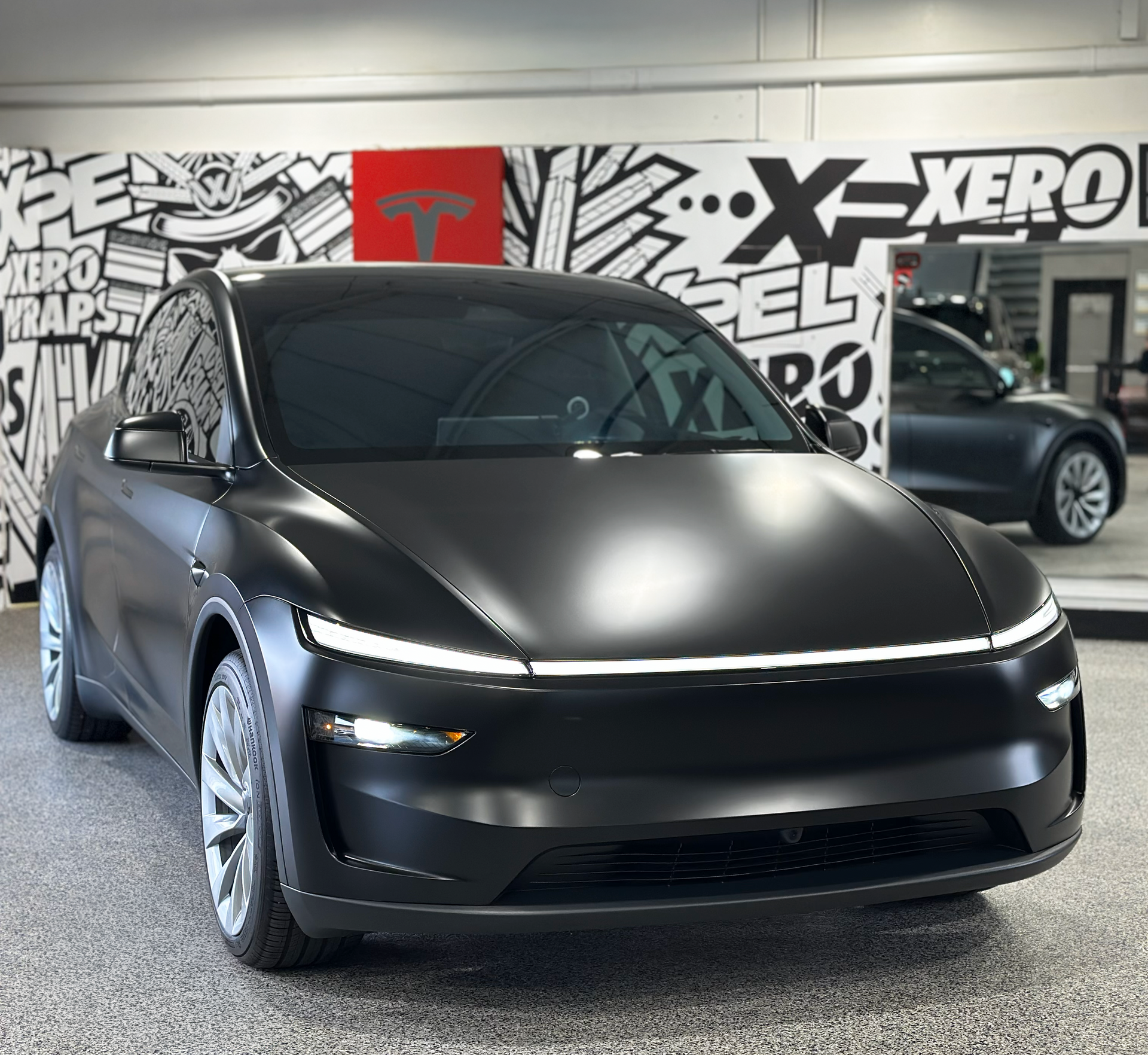 Black matte Tesla Model Y in a shop with black and white graphics.